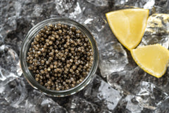 Jar of osetra caviar with lemon wedges on a dark surface